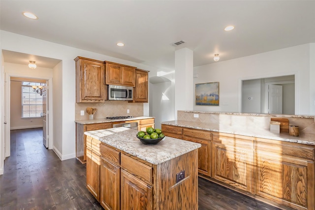 kitchen with a kitchen island, appliances with stainless steel finishes, dark hardwood / wood-style floors, backsplash, and light stone countertops