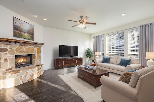 living room featuring a stone fireplace, dark hardwood / wood-style floors, and ceiling fan