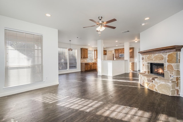 unfurnished living room featuring dark wood-type flooring, ceiling fan, and a stone fireplace