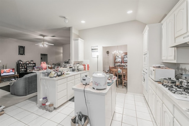 kitchen with white cabinetry, a center island, white appliances, light tile patterned floors, and ceiling fan with notable chandelier