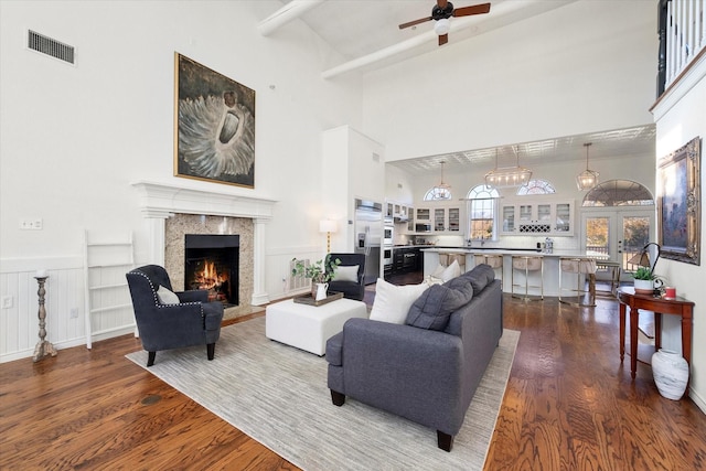 living room featuring a high ceiling, dark hardwood / wood-style flooring, beamed ceiling, a premium fireplace, and ceiling fan