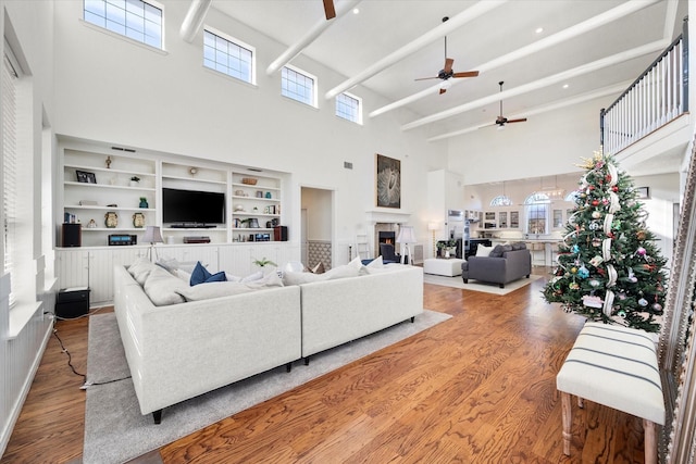 living room with a high ceiling, ceiling fan, built in features, and hardwood / wood-style flooring