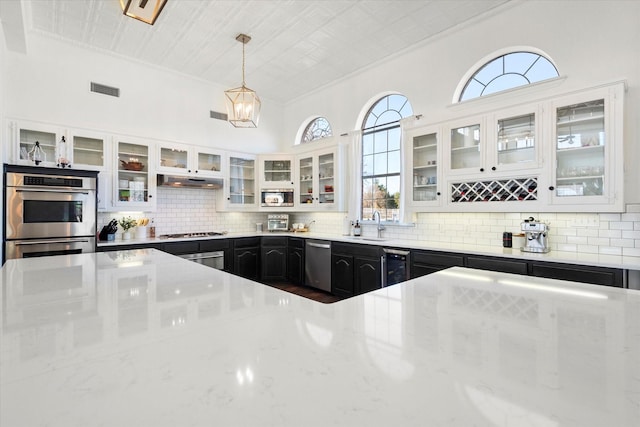 kitchen with light stone countertops, pendant lighting, white cabinetry, stainless steel appliances, and backsplash