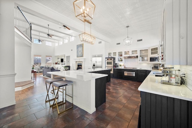 kitchen featuring a spacious island, hanging light fixtures, built in appliances, white cabinets, and a breakfast bar