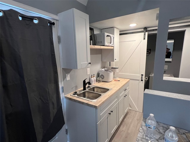 kitchen featuring sink, a barn door, light hardwood / wood-style flooring, and white cabinetry