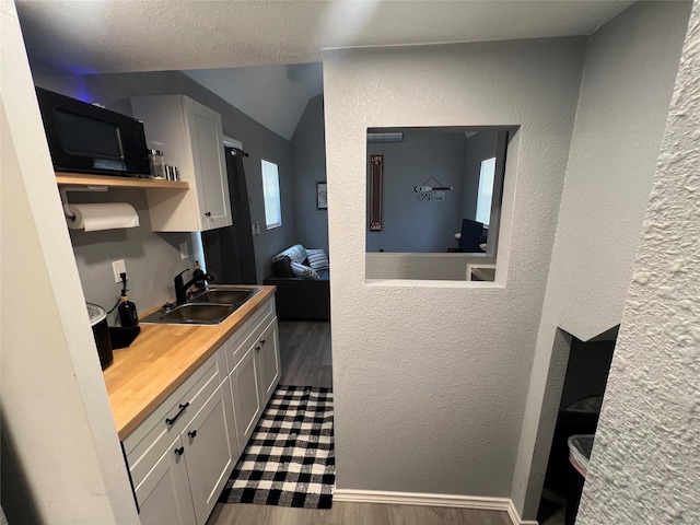 kitchen with lofted ceiling, wood counters, dark hardwood / wood-style flooring, white cabinets, and sink