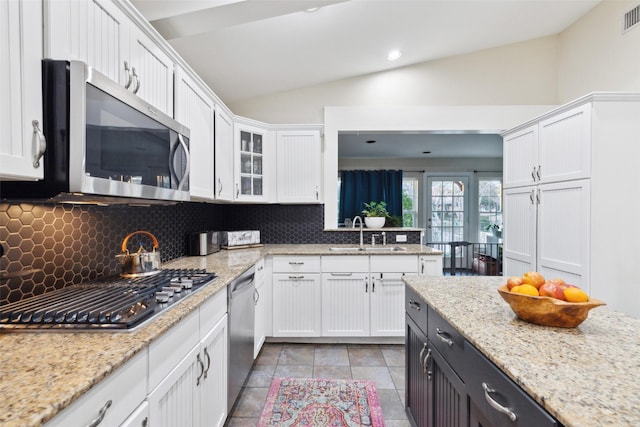 kitchen featuring vaulted ceiling, decorative backsplash, white cabinetry, appliances with stainless steel finishes, and sink