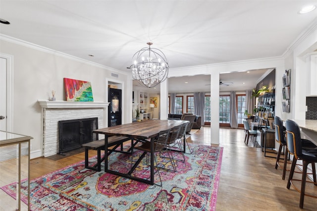 dining space with ceiling fan with notable chandelier, light hardwood / wood-style floors, crown molding, and a stone fireplace