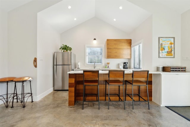 kitchen with kitchen peninsula, lofted ceiling, stainless steel refrigerator, a kitchen breakfast bar, and sink