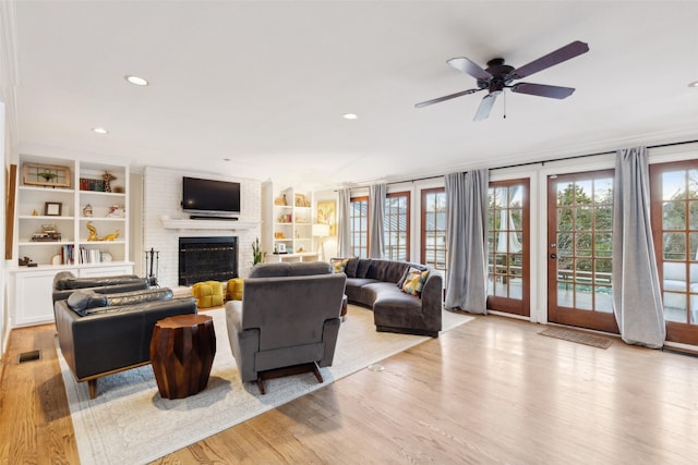 living room featuring a fireplace, built in features, ceiling fan, and light hardwood / wood-style flooring