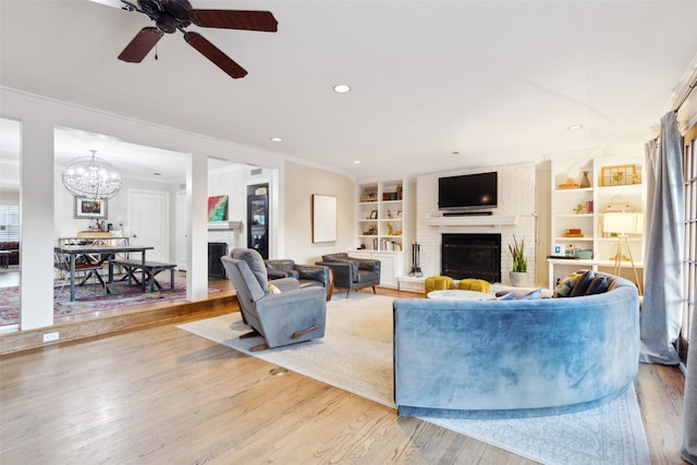 living room featuring ceiling fan with notable chandelier, a brick fireplace, crown molding, and built in features