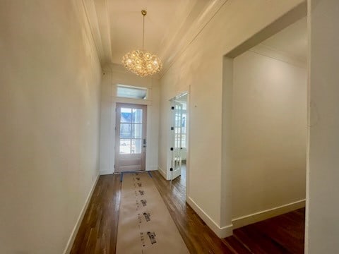 doorway to outside with an inviting chandelier, crown molding, and dark hardwood / wood-style floors