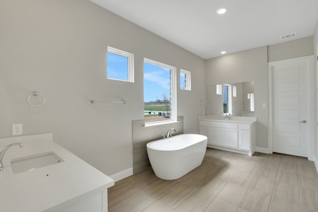 full bath with visible vents, two vanities, a sink, baseboards, and a soaking tub