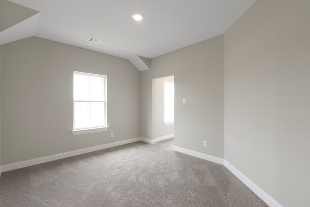 carpeted spare room with visible vents, baseboards, and lofted ceiling