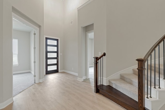 foyer entrance featuring visible vents, baseboards, light wood-style floors, a towering ceiling, and stairs