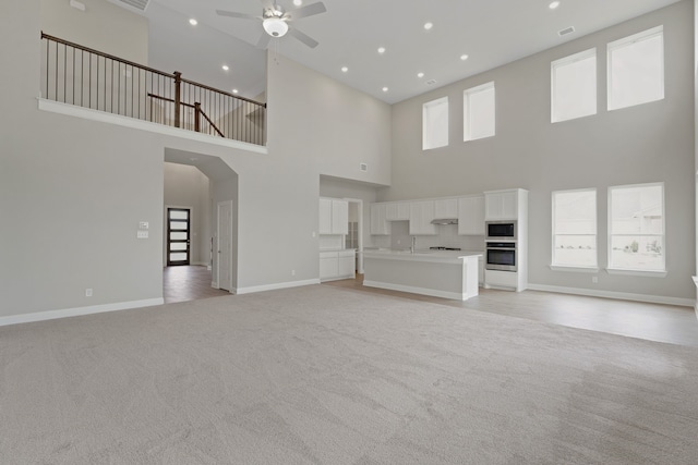 unfurnished living room featuring ceiling fan, baseboards, a wealth of natural light, and light carpet