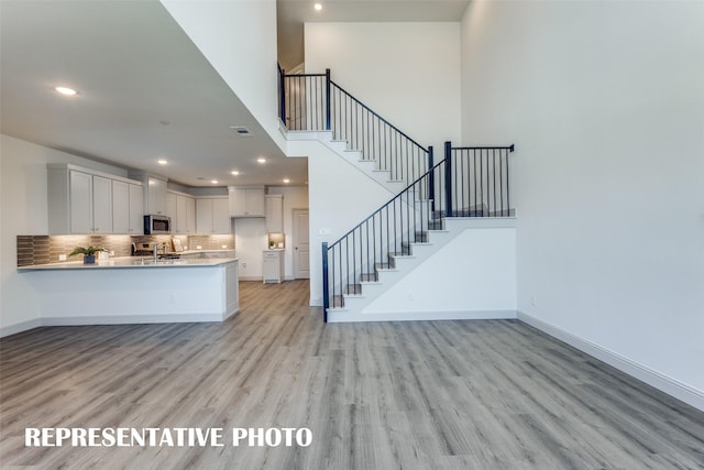 kitchen featuring stainless steel appliances, light wood-type flooring, kitchen peninsula, decorative backsplash, and white cabinets