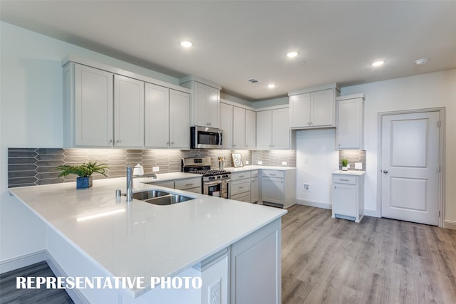 kitchen with kitchen peninsula, light hardwood / wood-style flooring, white cabinetry, appliances with stainless steel finishes, and sink