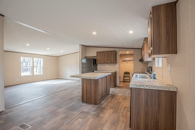 kitchen featuring dark wood-type flooring, a center island, black fridge, lofted ceiling, and sink