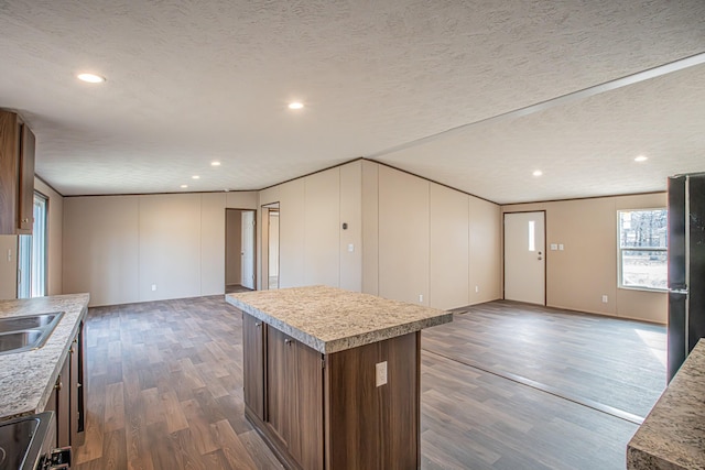 kitchen featuring a textured ceiling, dark hardwood / wood-style flooring, black refrigerator, and a kitchen island