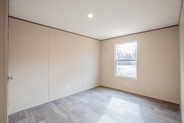 empty room with a textured ceiling, light wood-type flooring, and ornamental molding