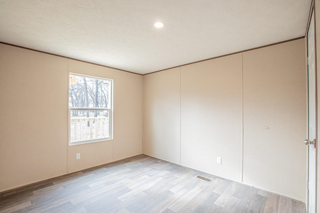 spare room featuring light wood-type flooring, ornamental molding, and a textured ceiling