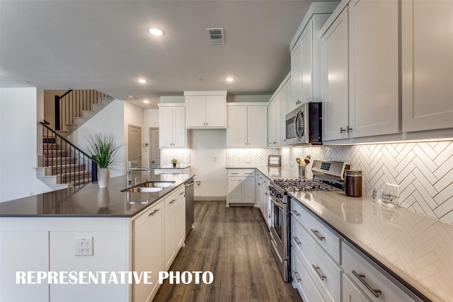 kitchen with sink, white cabinets, dark hardwood / wood-style floors, a kitchen island with sink, and appliances with stainless steel finishes