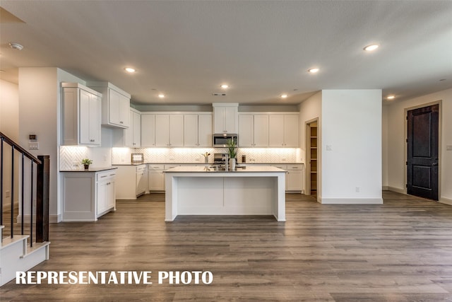 kitchen with a kitchen island with sink, appliances with stainless steel finishes, decorative backsplash, hardwood / wood-style flooring, and white cabinetry