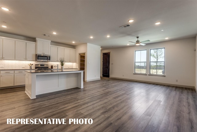 kitchen with appliances with stainless steel finishes, dark wood-type flooring, an island with sink, and white cabinetry