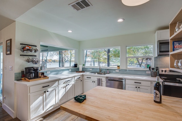 kitchen with a healthy amount of sunlight, stainless steel appliances, wooden counters, white cabinetry, and sink