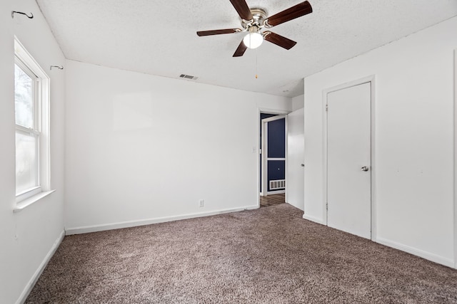 carpeted empty room with a textured ceiling, ceiling fan, and a wealth of natural light