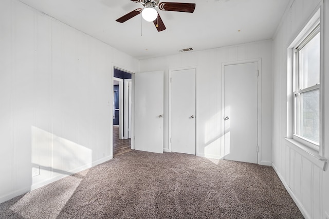 unfurnished bedroom with multiple closets, ceiling fan, and carpet