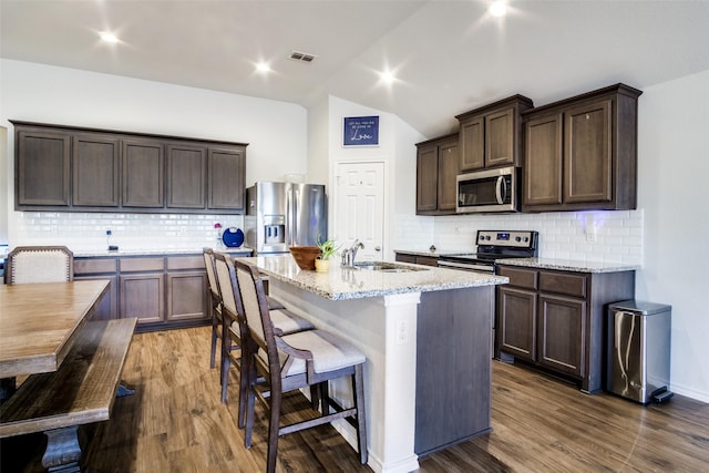 kitchen featuring dark hardwood / wood-style floors, a kitchen island with sink, backsplash, appliances with stainless steel finishes, and sink