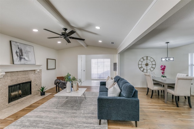 living room featuring light hardwood / wood-style floors, ceiling fan with notable chandelier, lofted ceiling with beams, and a fireplace