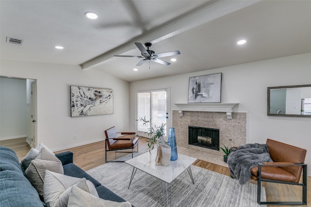 living room with vaulted ceiling with beams, ceiling fan, a tiled fireplace, and light wood-type flooring