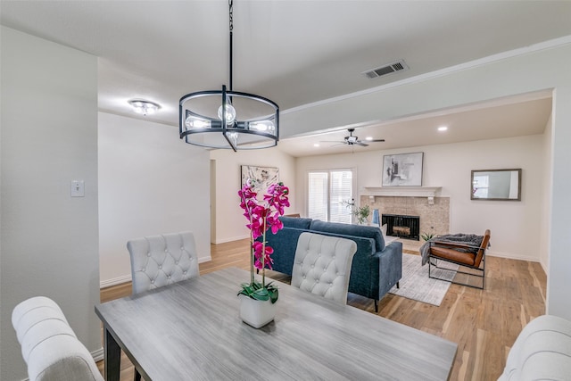 dining space with light wood-type flooring, ceiling fan with notable chandelier, and a fireplace