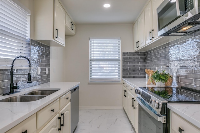 kitchen with white cabinetry, stainless steel appliances, light stone countertops, and sink