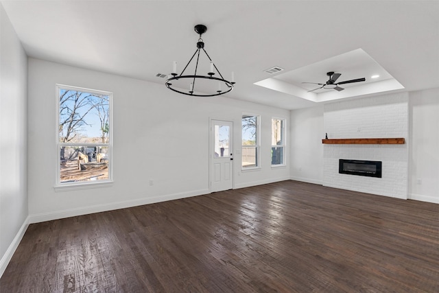 unfurnished living room featuring dark hardwood / wood-style floors, a brick fireplace, plenty of natural light, and a tray ceiling