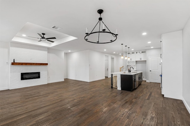 kitchen featuring a kitchen island with sink, hanging light fixtures, dark hardwood / wood-style floors, white cabinetry, and ceiling fan with notable chandelier