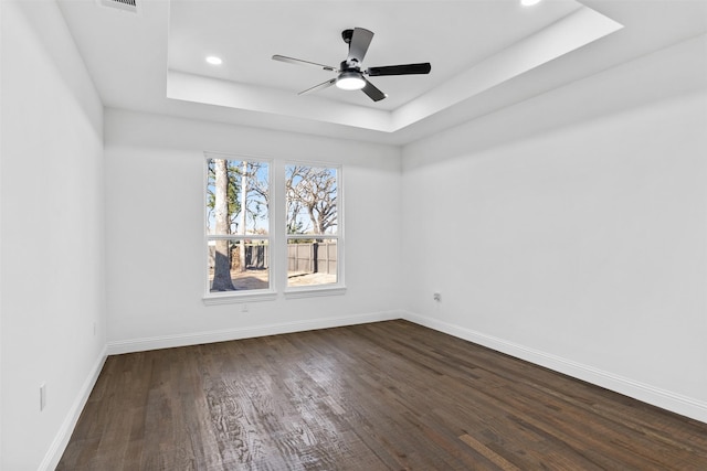 unfurnished room featuring dark wood-type flooring, a raised ceiling, and ceiling fan