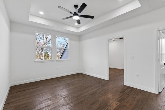 unfurnished room with a raised ceiling, ceiling fan, and dark hardwood / wood-style floors