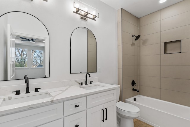 full bathroom with tiled shower / bath combo, wood-type flooring, toilet, vanity, and ceiling fan