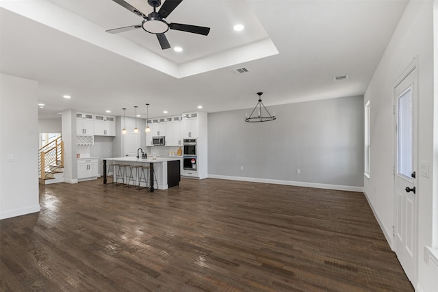 unfurnished living room featuring dark hardwood / wood-style flooring, ceiling fan, and a raised ceiling