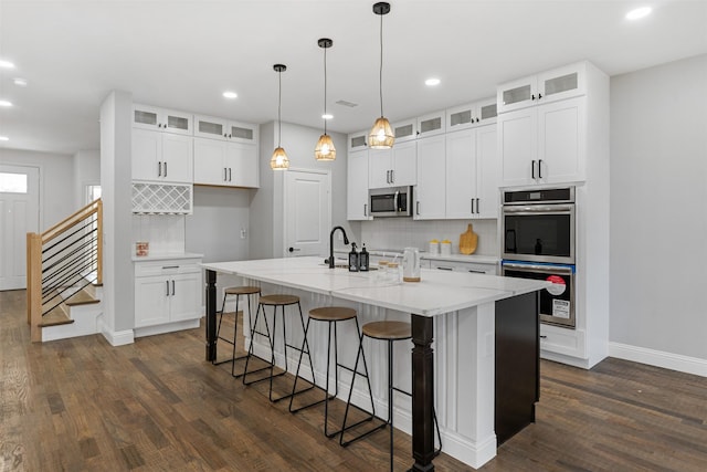 kitchen featuring stainless steel appliances, white cabinets, decorative backsplash, hanging light fixtures, and a center island with sink