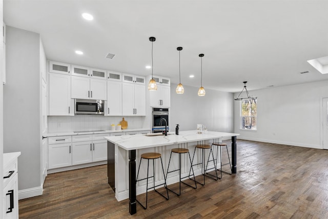 kitchen featuring appliances with stainless steel finishes, white cabinetry, a kitchen island with sink, and decorative backsplash