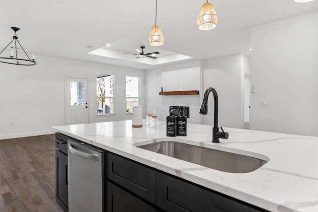 kitchen featuring light stone countertops, dishwasher, decorative light fixtures, a raised ceiling, and sink