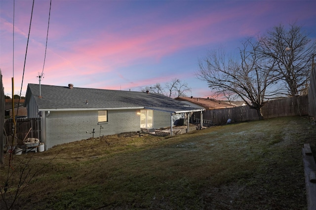 back house at dusk featuring a lawn