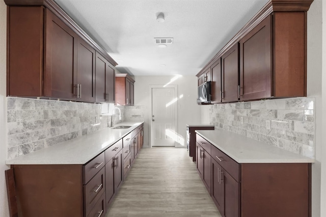 kitchen with tasteful backsplash, light wood-type flooring, dark brown cabinets, and sink