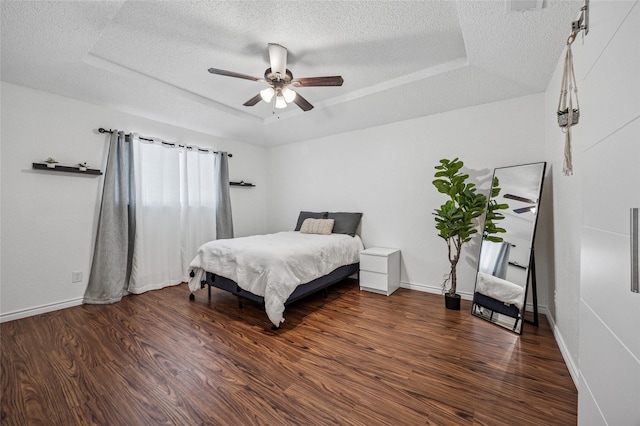 bedroom with ceiling fan, dark wood-type flooring, a textured ceiling, and a tray ceiling