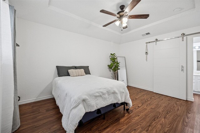 bedroom with a raised ceiling, a barn door, dark hardwood / wood-style floors, and ceiling fan